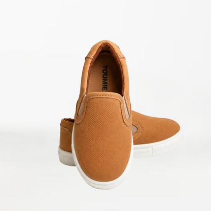 A pair of tan slip-on sneakers with white soles, shown from a rear three-quarter angle on a clean white background.