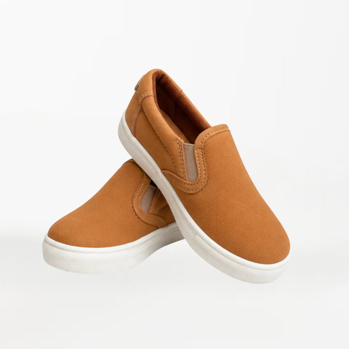 A pair of slip-on canvas sneakers in a warm camel brown color with white rubber soles, displayed on a clean white background.