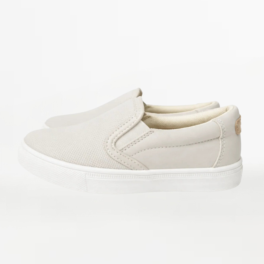 A pair of slip-on canvas sneakers in a light beige/off-white color, shown from a side profile view against a clean white background.