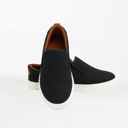 A pair of black slip-on canvas sneakers with white soles and a brown interior lining, displayed on a clean white background.