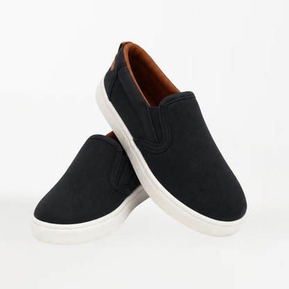 A pair of black slip-on canvas sneakers with white soles and a brown interior lining, displayed on a clean white background.
